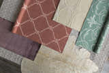 Close-up of Hazelhurst Area Carpet in dusty pink with a geometric pattern, light gray, and other rug samples. Styleshot