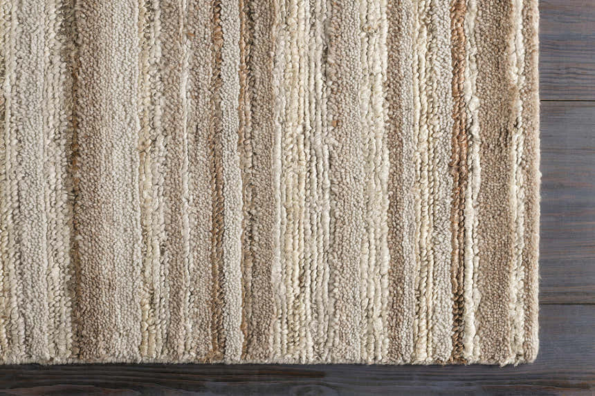 Close-up of the hand woven Greenbackvile Area Rug. Cream, beige, and brown jute and wool stripes on a dark wood floor. Corner