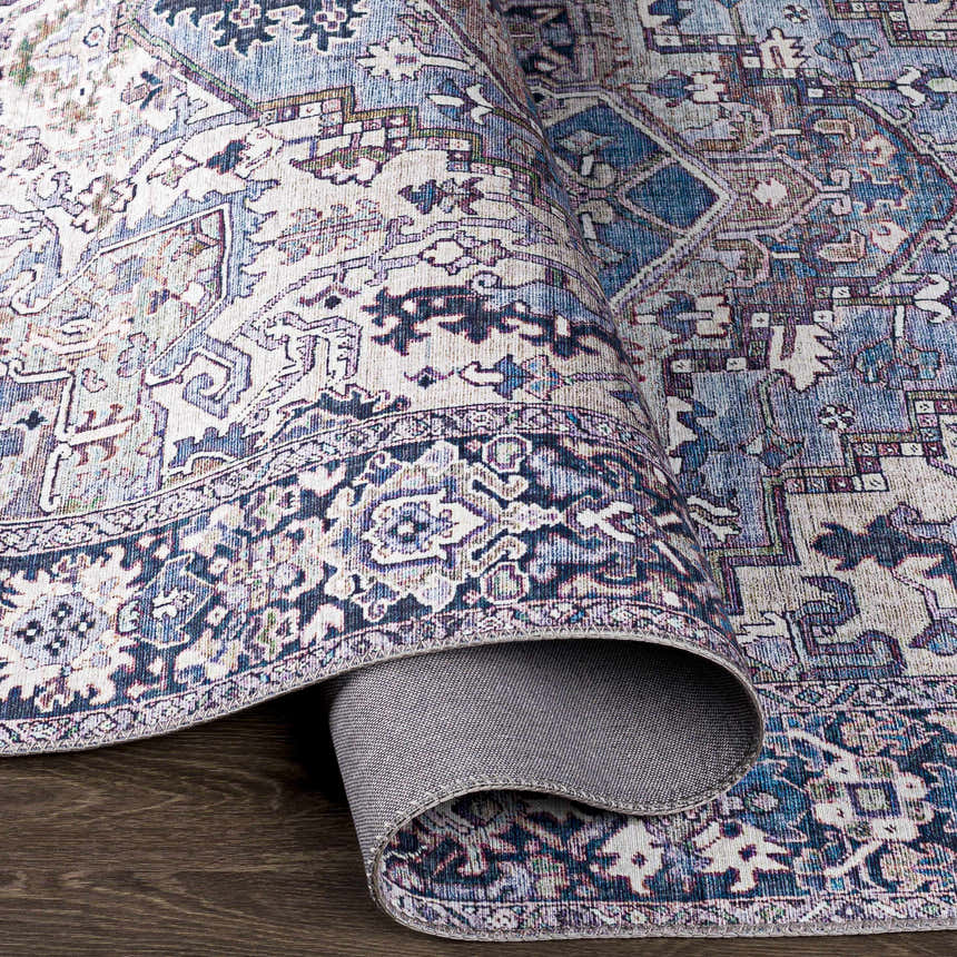 Close-up of the Neyland Iris Blue Area Rug. Features a traditional, bohemian pattern in cream, blue, and mauve tones. Fold