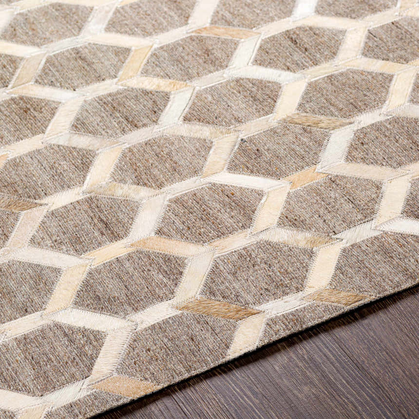 Close-up of the Haddix Premium Leather Rug. Features a beige and cream geometric pattern on a brown wood floor. Texture