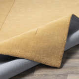 Close-up of the Bordered Solid Camel Yellow Wool Rug showing the texture, border detail, and backing. Fold