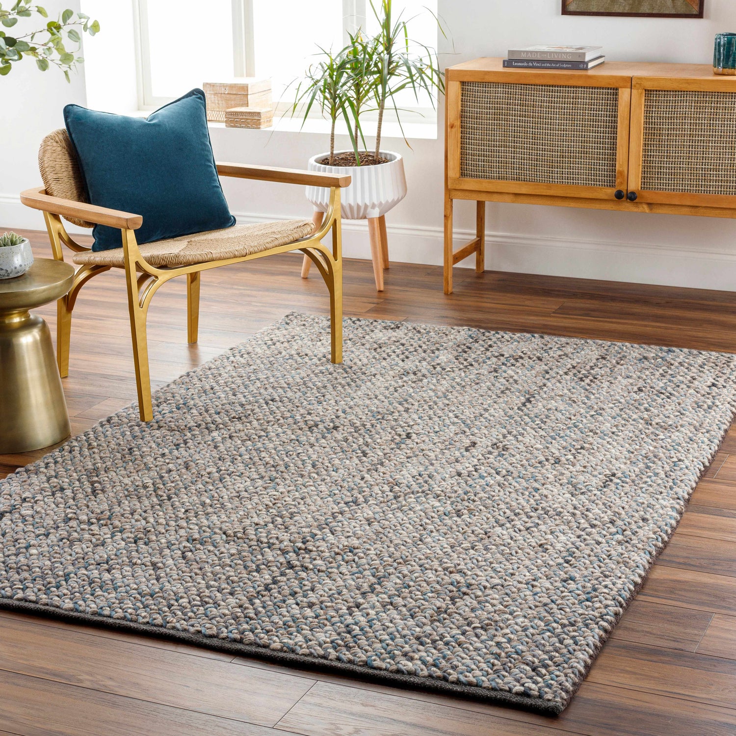 Living room scene with a charcoal, green, and ice blue Hansell Area Rug, woven chair, and wooden cabinet. Roomscene-Rectangle