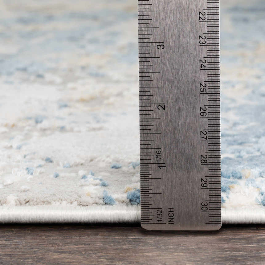 Close up of Hawes Faux Silk Rug showing texture and pile height with a ruler. Colors include light blue, gray, and mustard. Pile