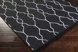 Close-up of the Hawthorne Indoor & Outdoor Rug. Black rug with a white geometric trellis pattern and fringe. Corner