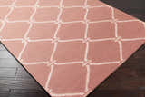 Close-up of Hazelhurst Area Carpet in dusty pink with a light gray geometric trellis pattern on dark wood floors. Corner