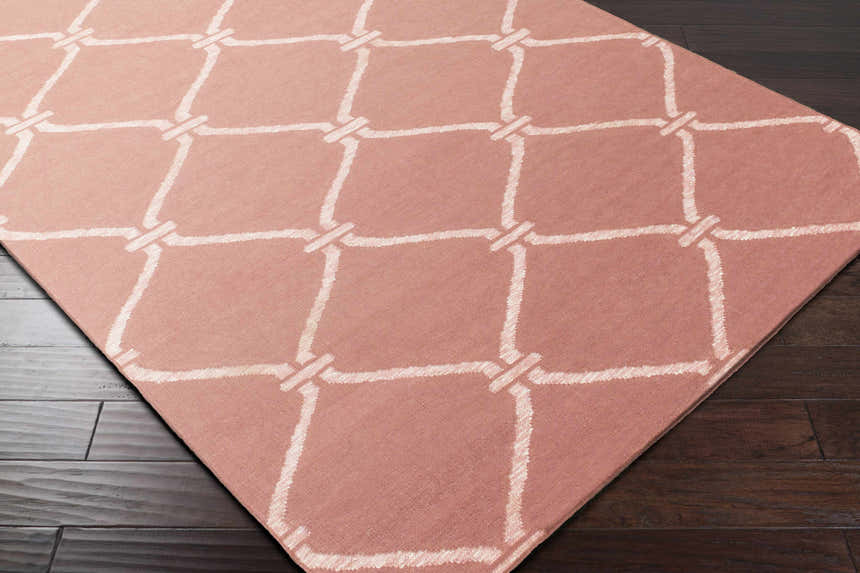 Close-up of Hazelhurst Area Carpet in dusty pink with a light gray geometric trellis pattern on dark wood floors. Corner