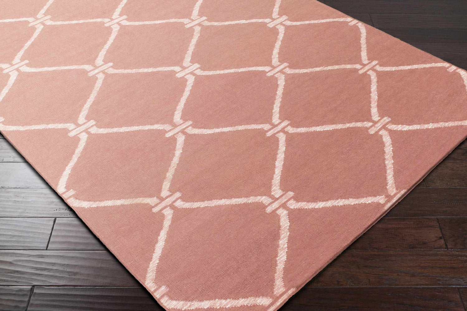 Close-up of Hazelhurst Area Carpet in dusty pink with a light gray geometric trellis pattern on dark wood floors. Corner