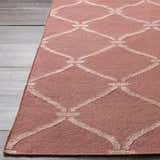 Close-up of a dusty pink Hazelhurst Area Carpet with a light gray diamond trellis pattern on a gray wood floor. Front