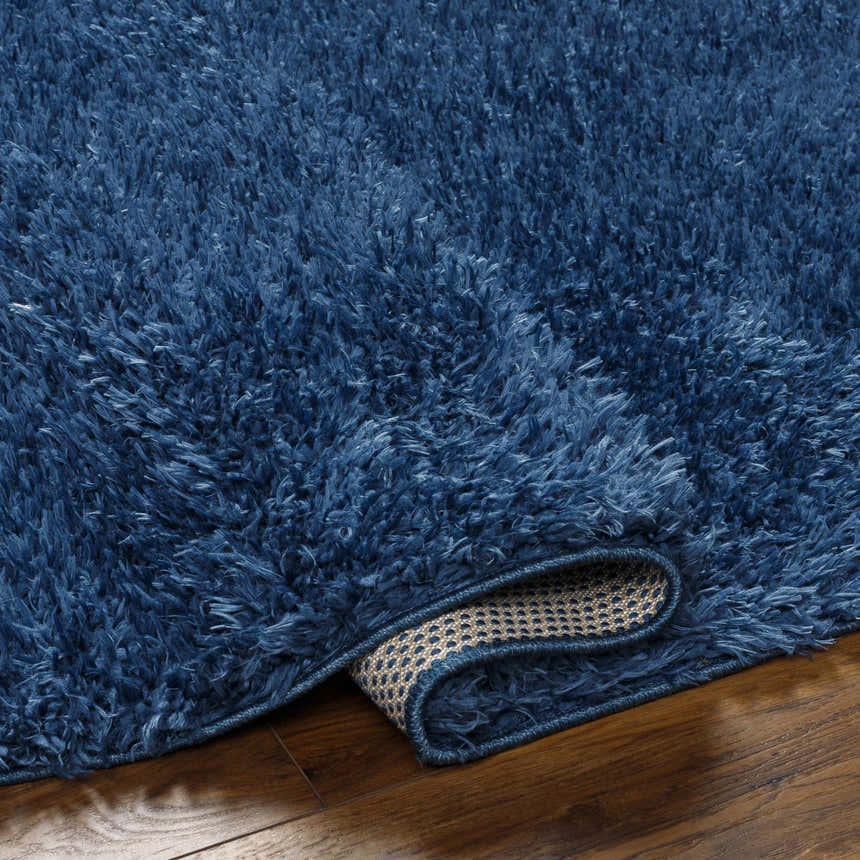 Close up of the plush Faina Solid Dark Blue Shag Washable Area Rug on hardwood flooring, showing the rug's backing. Fold