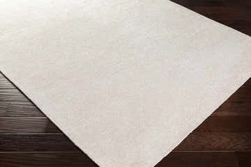 Close up of the ivory Hookstown Area Rug showing its hand woven texture on a dark wood floor. Corner