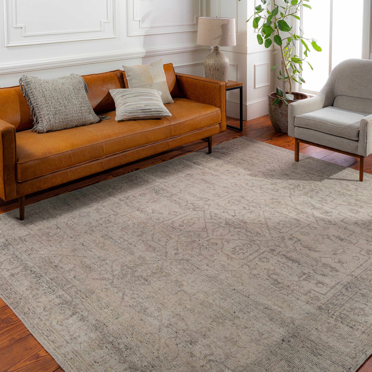 Living room scene with a beige Hollym Premium Rug, tan leather sofa, and light gray armchair. Roomscene-Rectangle