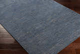 Close-up of the hand-knotted Hoole Area Rug. Dark blue wool rug with subtle off-white and tan pattern on dark wood floor. Corner