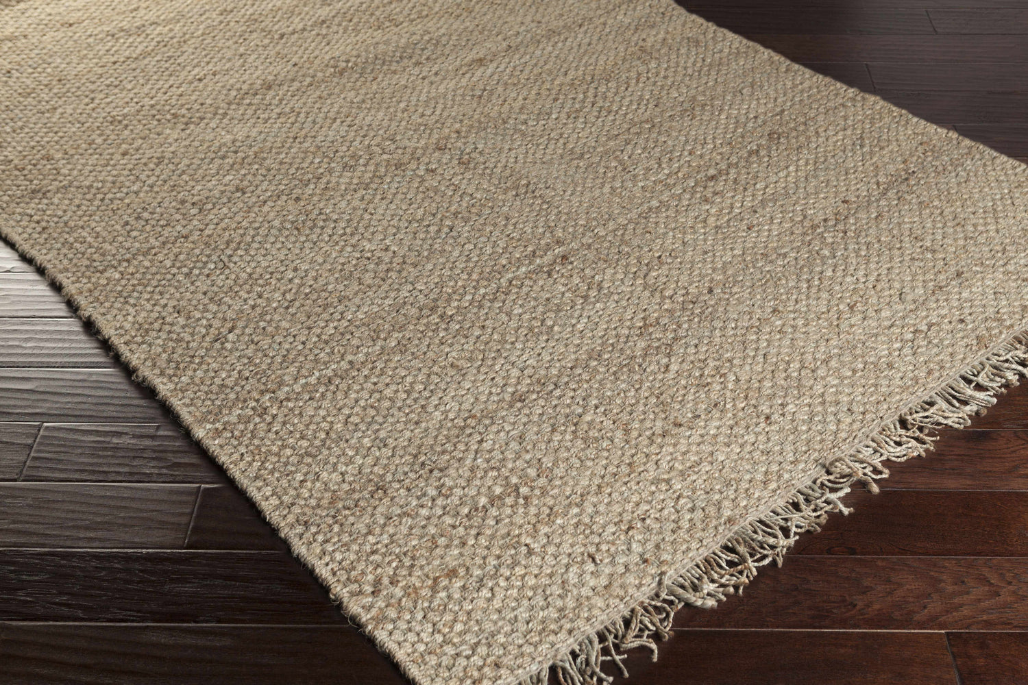 Close-up of Hovland Hand Woven Natural Jute Rag Rug showing natural jute color and fringe detail on dark hardwood floor. Swatch