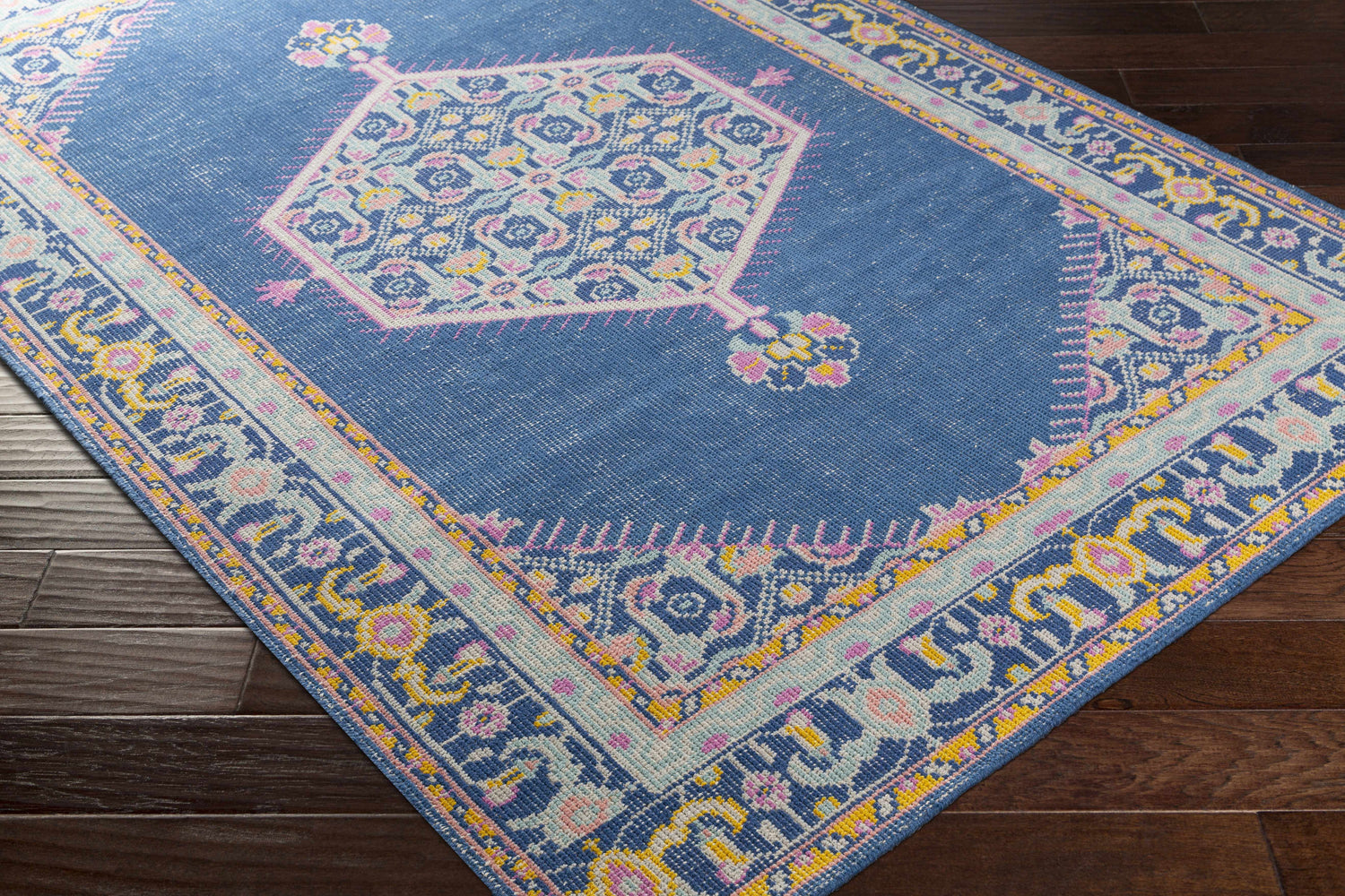 Close-up of the Herriman Clearance Rug. Hand-knotted wool rug in aqua, pink, saffron, and blue on dark wood floor. Corner