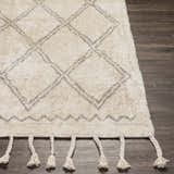 Close up of Harvester Area Carpet. Cream rug with gray geometric diamond pattern and braided tassels on dark wood floor. Front