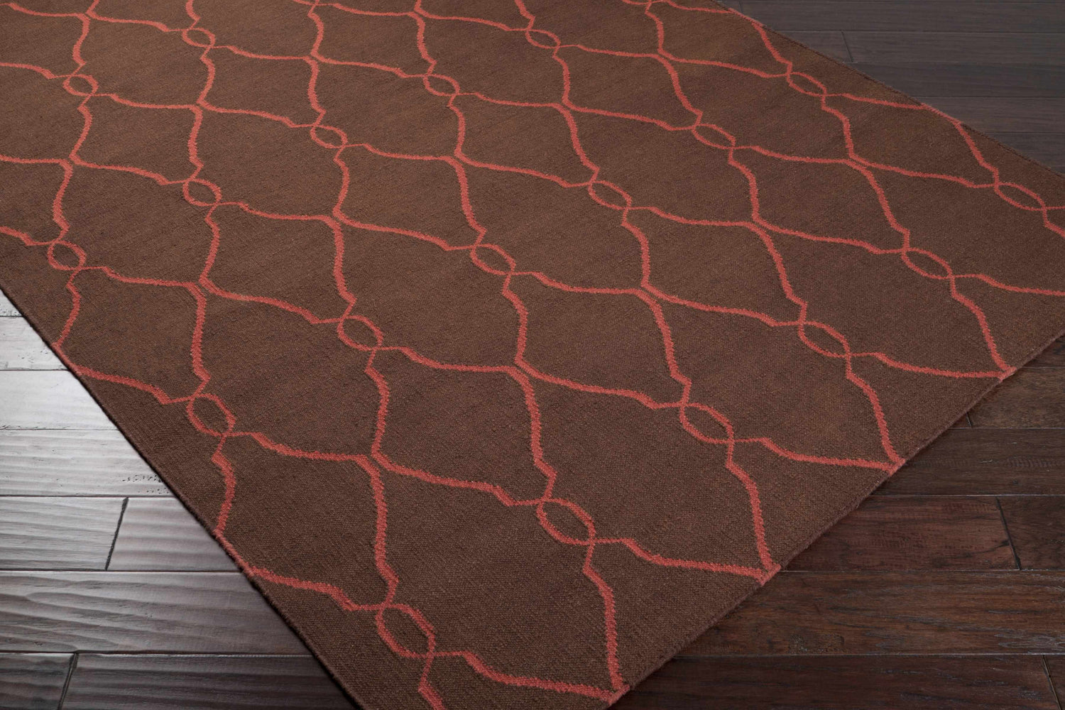 Humarock Area Rug, a hand-woven wool rug in burgundy and brown with a contemporary geometric trellis pattern. Corner