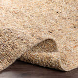 Close-up of the hand-woven Humbird Area Rug. The wool rug features a textured, looped pile in dark brown, red, peach, and tan tones. Fold