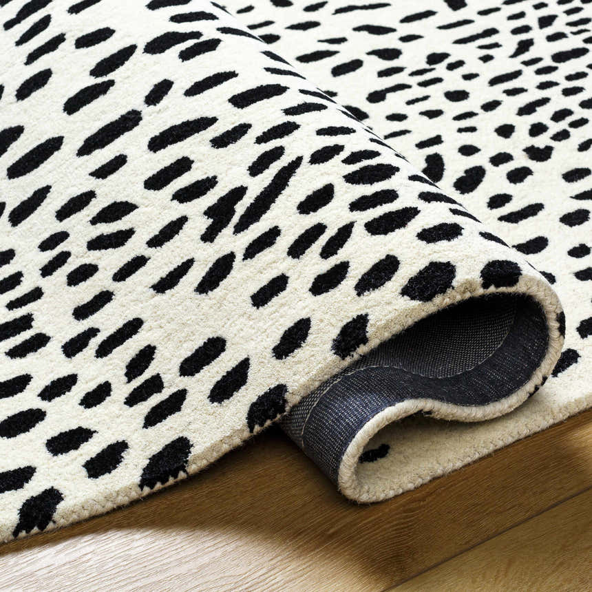 Close-up of the hand-tufted Athena White Giraffe Print Wool Rug with a black animal print design on an off-white background. Fold