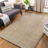 Living room scene with a black and beige Iqaluit Natural Jute Rug, gray sofa, plants, and wood floors. Roomscene-Rectangle
