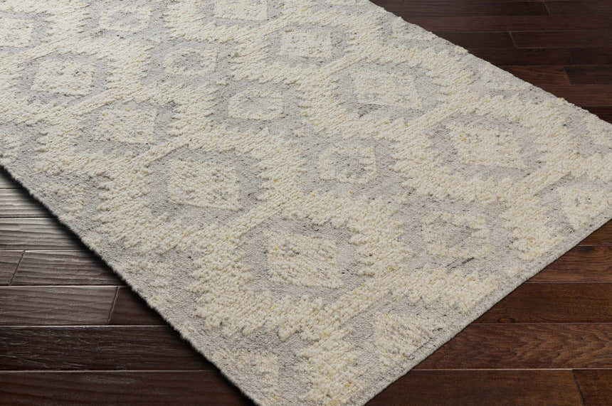 Close-up of the hand woven Jagupit Area Rug. Brown wood floors contrast with the cream and light gray wool rug. Corner
