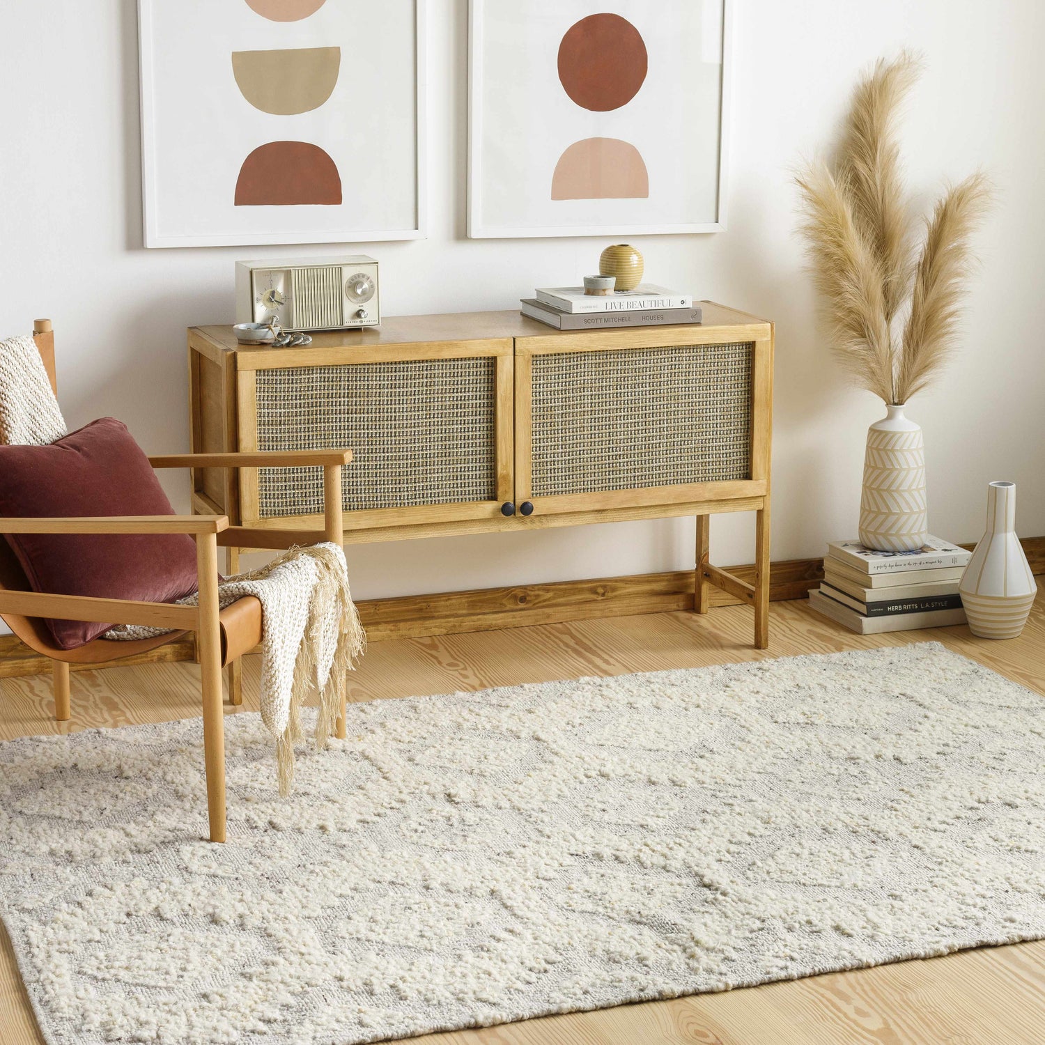Living room scene with a cream Jagupit Area Rug, wood cabinet, chair, and modern art. Bohemian, Scandinavian style. Roomscene-Rectangle