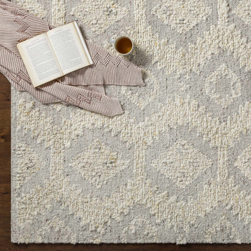Brown, cream Jagupit Area Rug with a geometric pattern. Styled with a book, blanket, and tea on a wood floor. Styleshot
