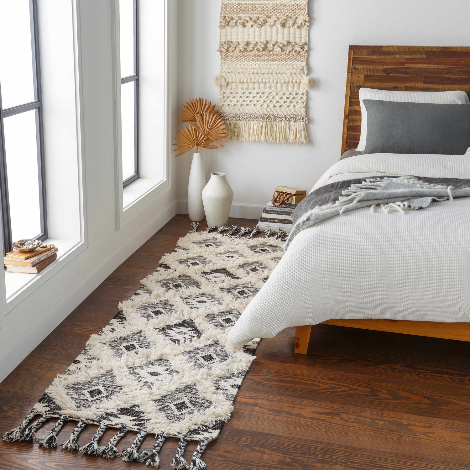 Bedroom scene with a Jarales Cream/Black Tribal Tassel Wool Rug runner, wood floors, and a bed with white bedding. Modern bohemian style. Roomscene-Runner