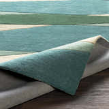 Close-up of the Jarratt Modern Wool Rug. Features a striped pattern in cream, teal, and sage green hues. Hand-tufted texture. Fold