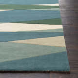 Close-up of the Jarratt Modern Wool Rug. Features a geometric pattern in cream, sage, green, and teal on dark wood flooring. Front