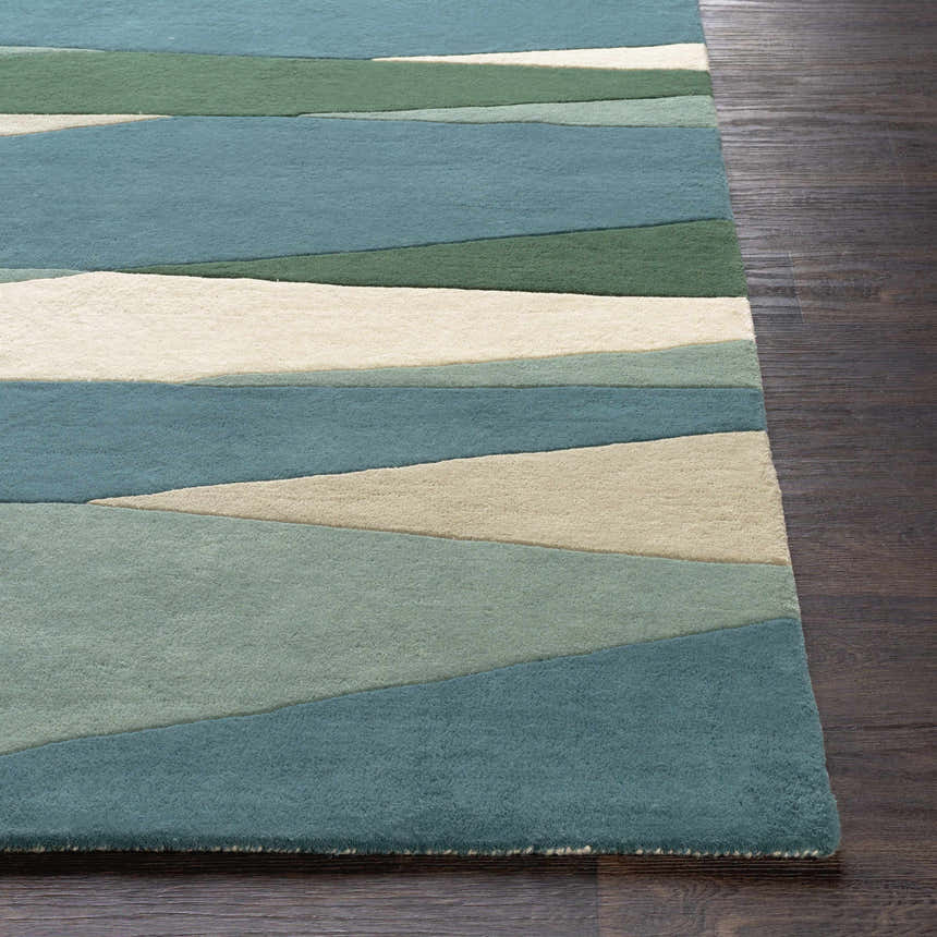 Close-up of the Jarratt Modern Wool Rug. Features a geometric pattern in cream, sage, green, and teal on dark wood flooring. Front