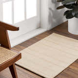 Entryway scene with a tan Javon Area Rug, wood floors, white door, and a mid-century modern chair. Roomscene-Rectangle