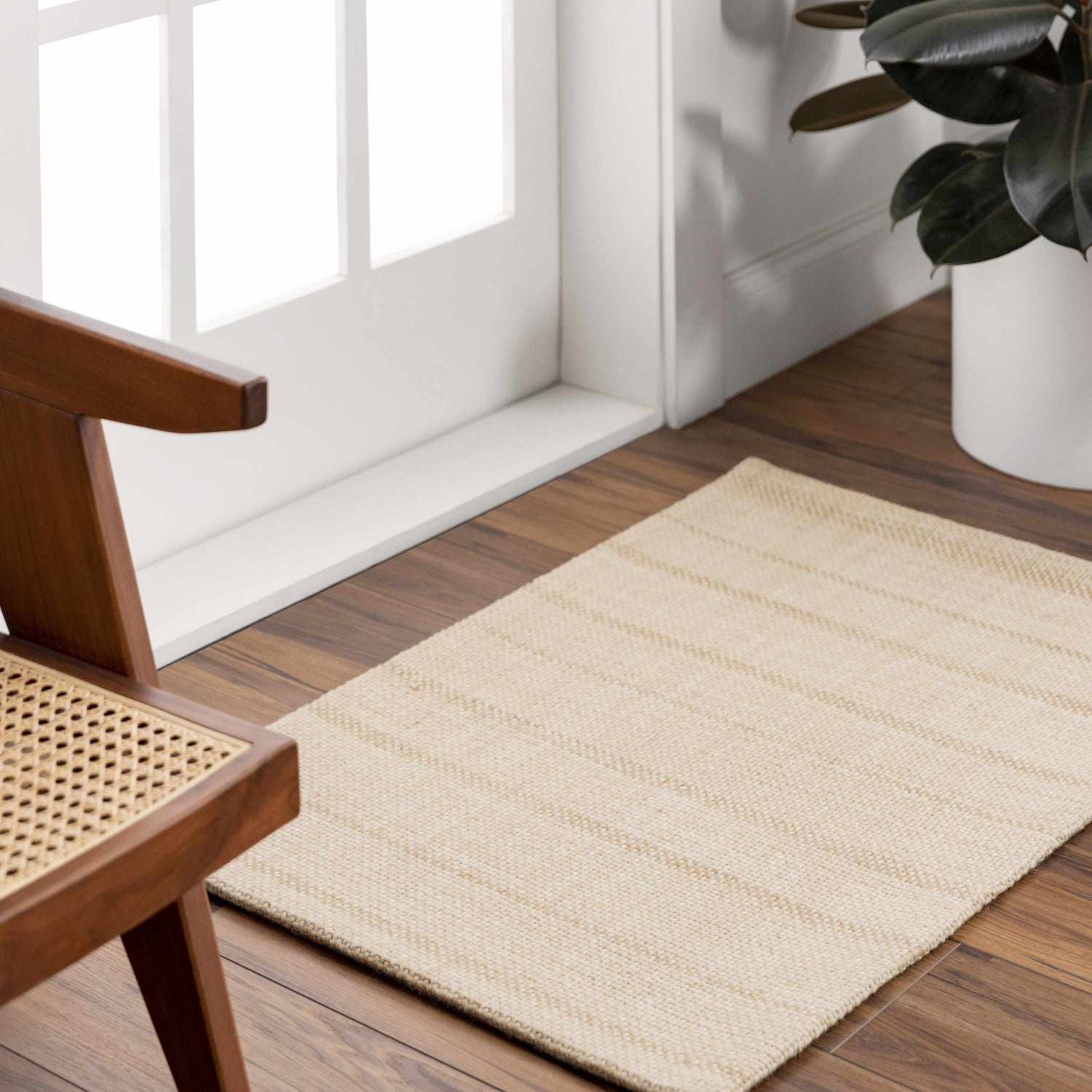 Entryway scene with a tan Javon Area Rug, wood floors, white door, and a mid-century modern chair. Roomscene-Rectangle