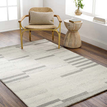 Modern living room scene with a beige Jeri Modern Wool Rug, woven chair, and wood side table. Roomscene-Rectangle