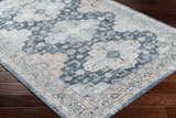 Close-up of the Jara Washable Area Rug. Traditional design in dark gray, denim, light gray, and nutmeg on dark wood floor. Corner