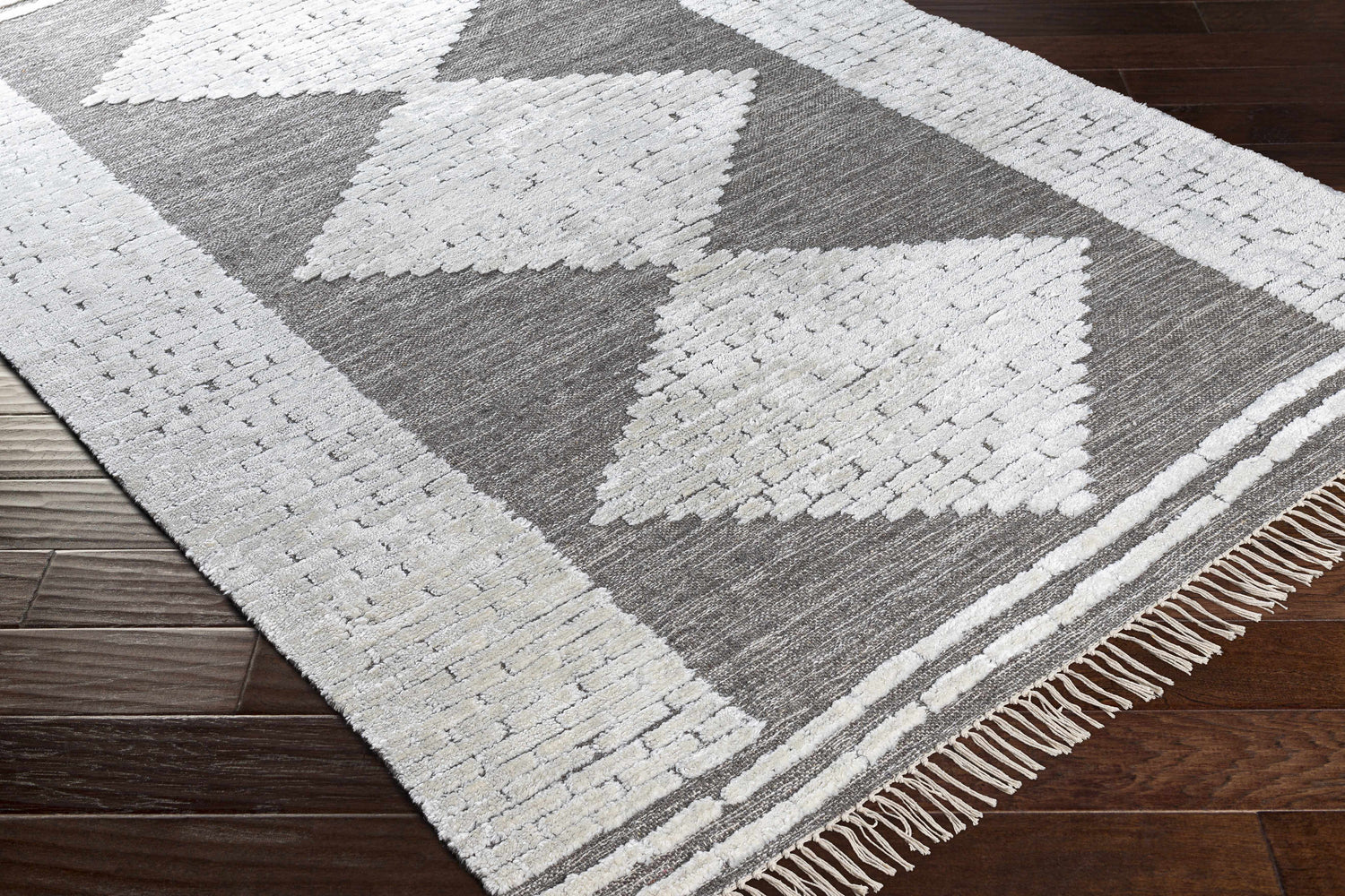 Close-up of the hand woven Junction Carpet. Brown and light beige geometric pattern with fringe detail. Corner