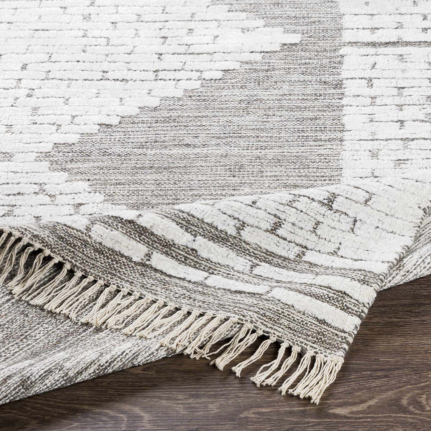Close up of the Junction Carpet, a brown and white hand woven rug with a geometric pattern and fringed edge. Fold