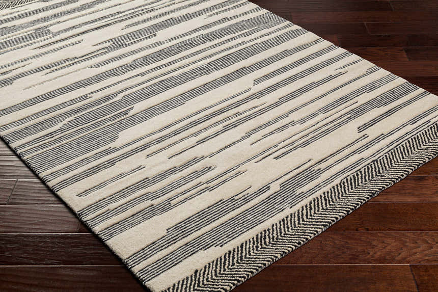 Close-up of the hand-tufted Jay Area Rug. Cream and black wool rug with geometric stripe pattern and chevron border. Corner