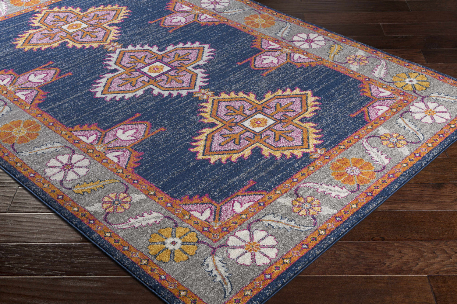 Close-up of Kaitlyn Navy Area Rug. Features a traditional floral and geometric design in navy, orange, and gray. Corner