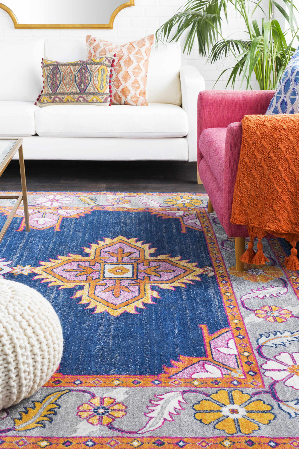 Living room scene with a Kaitlyn Navy Area Rug, white sofa, pink chair, and colorful pillows. Styleshot
