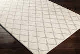 Close-up of the hand woven Kanopolis Carpet. Cream rug with a medium gray geometric diamond pattern. Corner