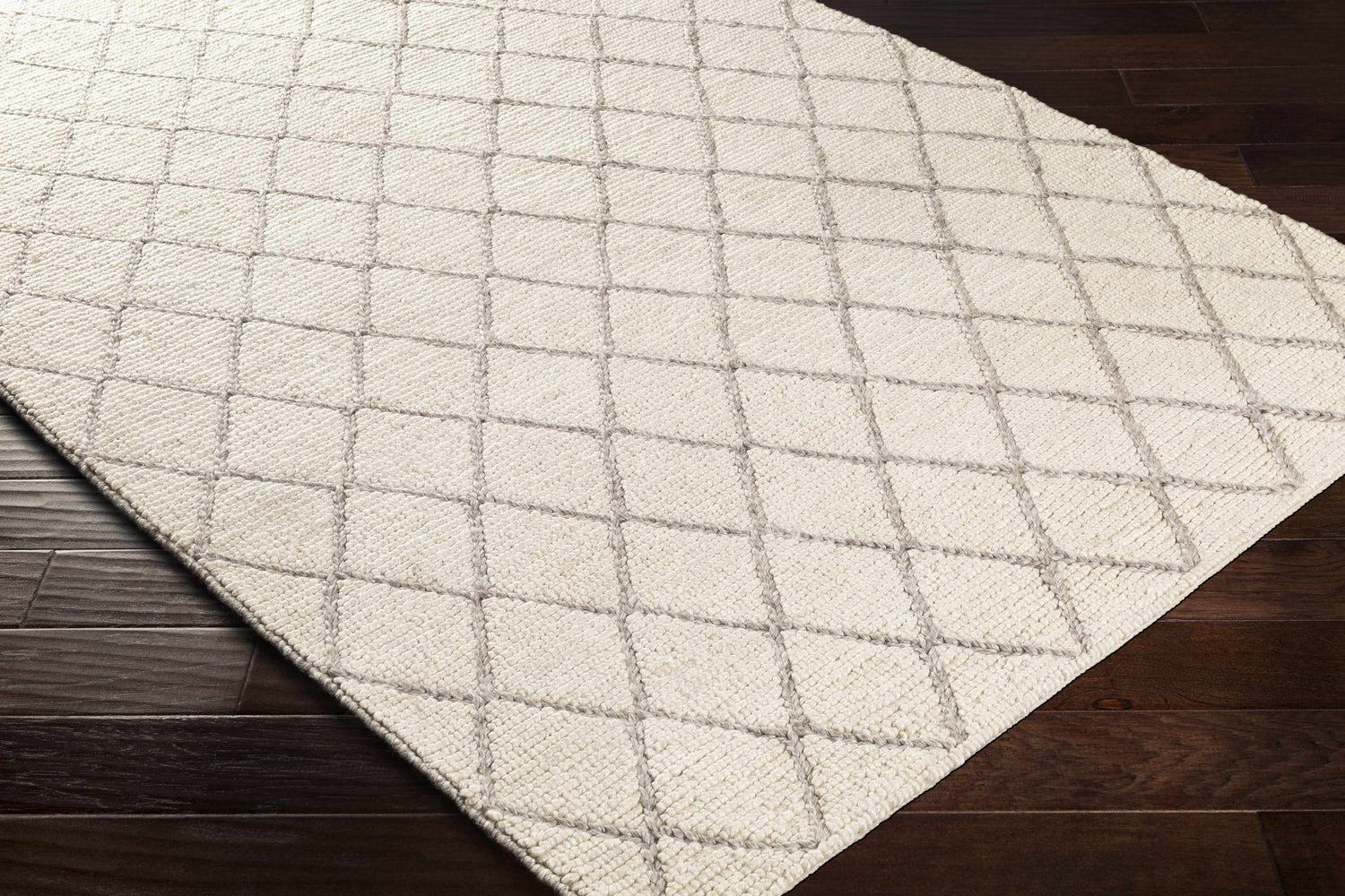 Close-up of the hand woven Kanopolis Carpet. Cream rug with a medium gray geometric diamond pattern. Corner