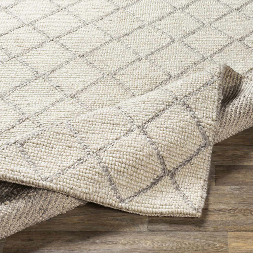 Close-up of the hand woven Kanopolis Carpet. Cream rug with medium gray diamond pattern and textured wool blend. Fold