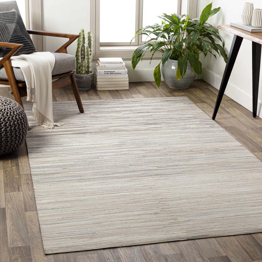 Living room scene with a beige Karabar Premium Area Rug, gray chair, and potted plant. Roomscene-Rectangle