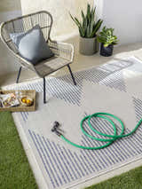 Outdoor patio scene with a cream and navy geometric Khandallah Area Rug, wicker chair, and garden hose. Roomscene-Rectangle