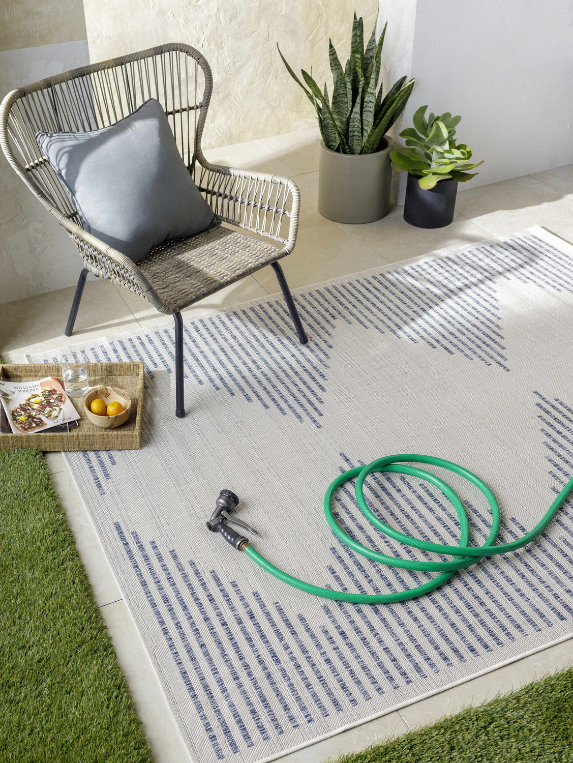 Outdoor patio scene with a cream and navy geometric Khandallah Area Rug, wicker chair, and garden hose. Roomscene-Rectangle