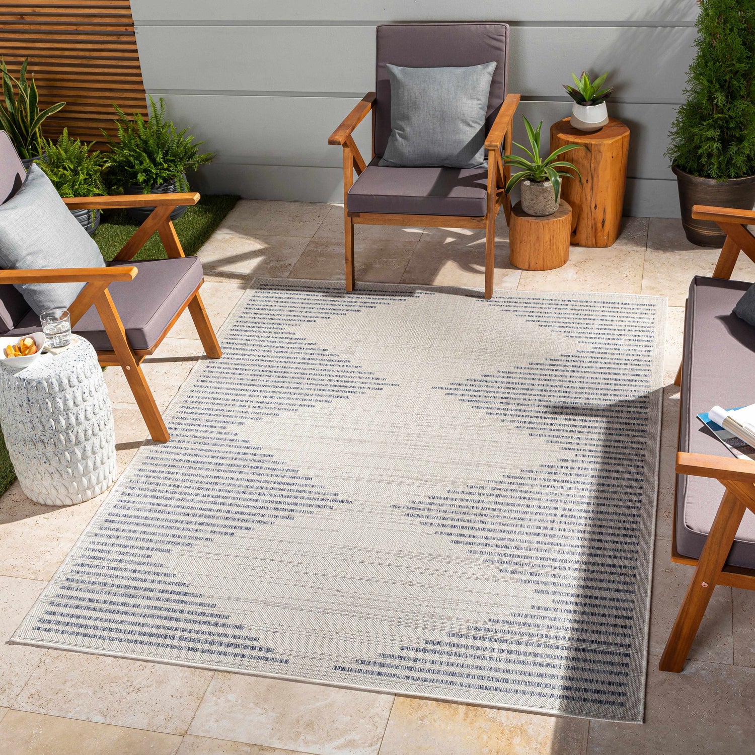 Outdoor patio scene with a cream and navy geometric Khandallah Area Rug, wood chairs, and stone tile flooring. Roomscene-Rectangle