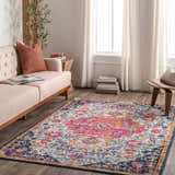 Living room scene with a Kialla Magenta & Burnt Orange Area Rug, light beige sofa, wood accents, and bright natural light. Roomscene-Rectangle