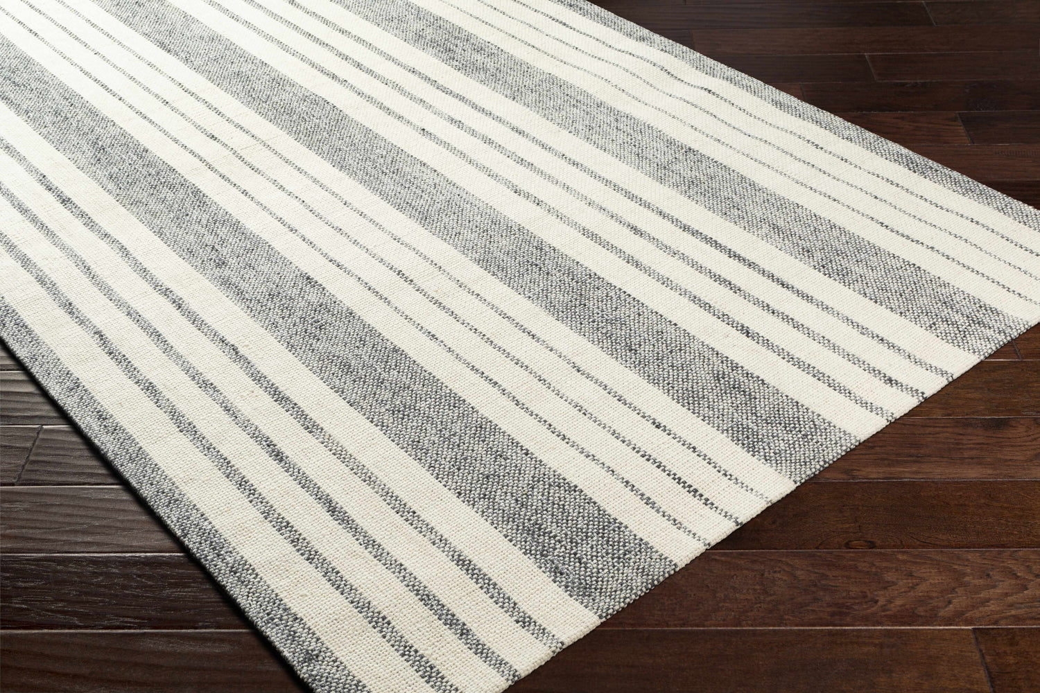 Close-up of the Kilmore Area Rug. Gray and white striped, hand-woven rug on dark wood flooring. Corner