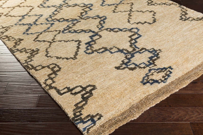 Close-up of the beige Kinards Jute Carpet with dark blue and ink blue geometric pattern on a dark wood floor. Corner
