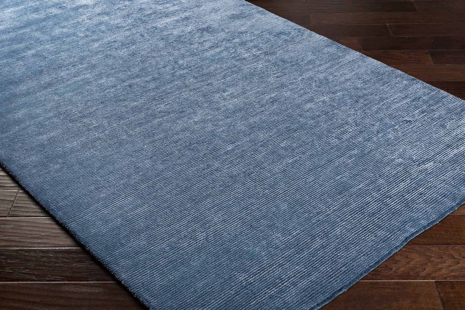 Close-up of the blue Kendall Carpet showing its hand-knotted texture and subtle pattern on dark wood flooring. Corner